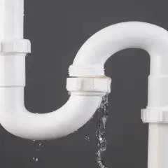 Tuyau de PVC blanc avec une fuite d'eau. Le temps de séchage de la colle PVC est crucial pour éviter ce genre de problème.