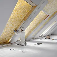 Un ouvrier installe un isolant en fibre de verre jaune dans un grenier.