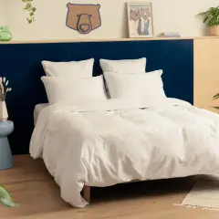 Une chambre adulte avec une tête de lit bicolore, bleu marine et bois clair. Le lit est fait de draps blancs immaculés.