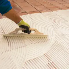 Main tenant, pose carrelage 60x60. Un artisan étale la colle avec une truelle pour préparer la pose de grands carreaux.