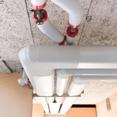 Gros tuyaux blancs, certains avec des capuchons rouges, sont installés sous un plafond texturé. L'ensemble est conçu pour isoler le tuyau de chauffage.