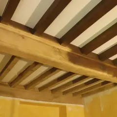 Poutres en bois brutes, prêtes pour le sablage, soutenant un plafond blanc. La texture naturelle du bois est visible.