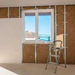 Travaux d'isolation intérieure : murs en cours de pose, avec laine de bois visible derrière une ossature métallique et une plaque de plâtre. Une échelle est présente.