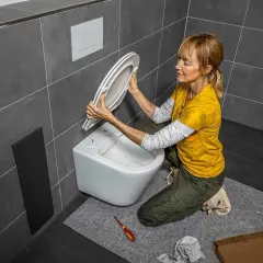Une femme s'apprête à changer l'abattant WC. Elle tient le nouvel abattant, prête à l'installer sur la cuvette.