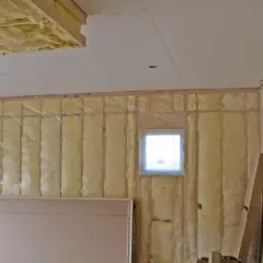 Isolation plafond garage en cours, murs recouverts de laine de verre et pare-vapeur. Deux petites fenêtres laissent passer la lumière.