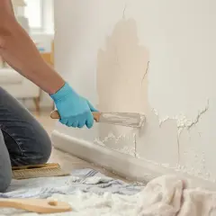 Un artisan répare une fissure sur un mur intérieur avec une spatule.