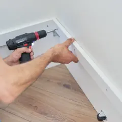 Un bricoleur utilise une visseuse pour fixer du placo sous pente, créant ainsi un espace de rangement fonctionnel.