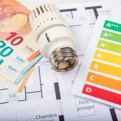 Billets en euros, thermostat et étiquette énergie sur un plan de maison. Un audit énergétique de maison pour optimiser les dépenses.