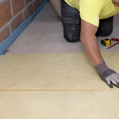 Pose d'une isolation sous dalle béton terre-plein. Un ouvrier ajuste un panneau isolant jaune.