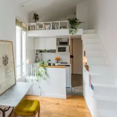 Un petit appartement optimisé pour le rangement, avec une cuisine, un coin repas et des escaliers menant à une mezzanine.