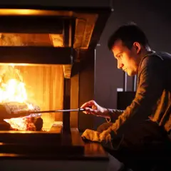 Un homme ajuste des bûches dans un poêle à bois, le feu crépite. Le tirage est parfait pour une soirée chaleureuse.