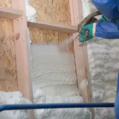 Application de polyuréthane projeté pour isoler une structure en bois. La mousse blanche s'étend, créant une barrière isolante.
