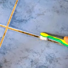 Main tenant, une brosse à dents verte et jaune est utilisée pour nettoyer joint salle de bain.