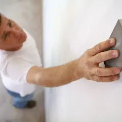 Un homme ponce un mur blanc avec une cale à poncer, préparant la surface avant de peindre.
