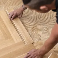 Pose d'un parquet flottant en chevrons. Un artisan applique la colle sur le sol avant de placer les lames de bois.