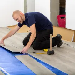 Pose d'un revêtement de sol stratifié sur une isolation sous carrelage. L'homme pose une lame de parquet.