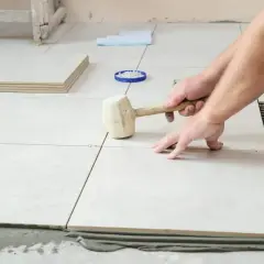 Pose de carrelage : un artisan utilise un maillet pour ajuster une nouvelle dalle sur le mortier.