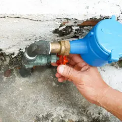 Main tenant intervient pour réparer une fuite d'eau sur un raccord de compteur.