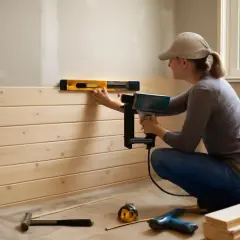 Une personne utilise un pistolet à clous et un niveau pour installer du **matériel placo** en lambris de bois.