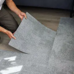 Pose d'une nouvelle moquette en dalles grises, recouvrant un ancien sol. Un homme pose une dalle, le geste est précis, comme s'il s'agissait de carreler sur du carrelage.