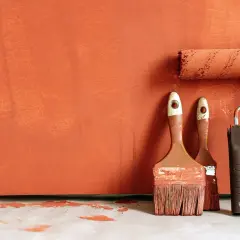 Pinceaux et rouleau de peinture orange sur fond texturé. Idéal pour savoir comment rattraper une peinture mal faite.