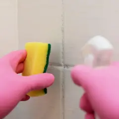Main rose gantée tient une éponge jaune pour nettoyer une tache sur carrelage qui ne part pas.