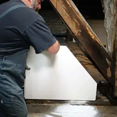 Un ouvrier installe un cloison carreau de plâtre blanc près d'une poutre en bois ancienne.