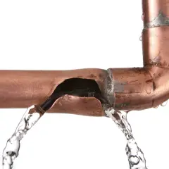 Une fuite sur un tuyau en cuivre provoque un jet d'eau. L'eau s'échappe d'une fissure béante dans le métal.