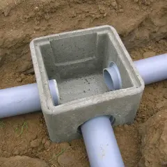 Pose regard béton pour l'eau pluviale, avec des tuyaux gris en PVC installés dans la terre.