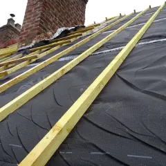Charpente en cours d'installation, avec la membrane d'étanchéité noire prête pour l'isolation toiture. Les chevrons en bois sont posés.