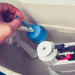 Main tenant ajuste le flotteur bleu pour arrêter la chasse d'eau qui coule.