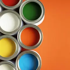 Un assortiment de pots de peinture glycero ou acrylique ouverts, révélant des couleurs vives comme le bleu, le jaune, le rouge, le vert et l'orange sur fond orange.