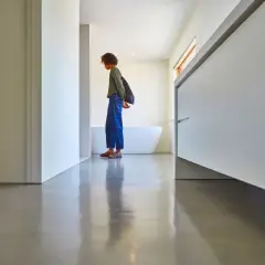 Une personne se tient sur un sol en béton ciré brillant, devant une baignoire et des meubles de salle de bain modernes.