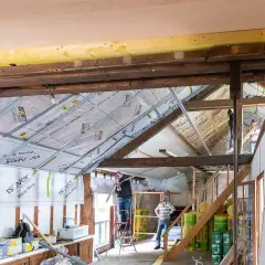 Travaux en cours pour refaire un plafond. Des ouvriers installent des rails métalliques sous les poutres apparentes.