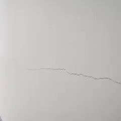 Un fin mur qui s'effrite, marqué par une longue fissure sinueuse, témoigne du passage du temps dans un couloir lumineux.