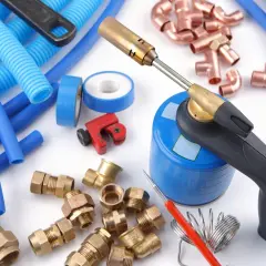 Outils pour une installation multicouche : chalumeau, tubes bleus, raccords en laiton et cuivre, coupe-tube.