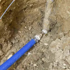 Raccordement d'une canalisation eau enterrée, respectant les normes. Le tuyau bleu est relié à une conduite plus ancienne.