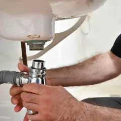 Main tenant en main le siphon, il procède au démontage du siphon de la baignoire pour une réparation.