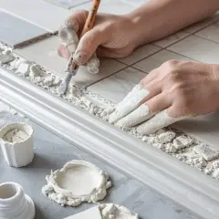 Mains gantées de poudre, on applique le joint plinthe carrelage avec soin. Outils et matériaux à portée de main pour un travail de précision.