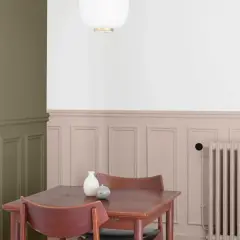 Peinture salon deux tons : mur vert olive contrastant avec un soubassement rose poudré orné de moulures. Une table en bois et des chaises sont disposées près d'un radiateur.