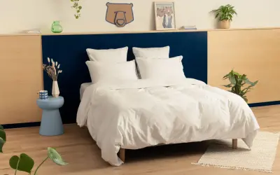 Une chambre adulte avec une tête de lit bicolore, bleu marine et bois clair. Le lit est fait de draps blancs immaculés.
