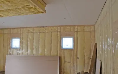 Isolation plafond garage en cours, murs recouverts de laine de verre et pare-vapeur. Deux petites fenêtres laissent passer la lumière.
