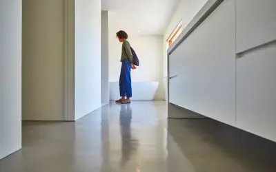 Une personne se tient sur un sol en béton ciré brillant, devant une baignoire et des meubles de salle de bain modernes.