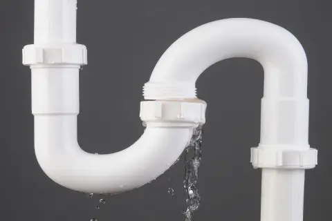 Tuyau de PVC blanc avec une fuite d'eau. Le temps de séchage de la colle PVC est crucial pour éviter ce genre de problème.