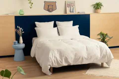 Une chambre adulte avec une tête de lit bicolore, bleu marine et bois clair. Le lit est fait de draps blancs immaculés.