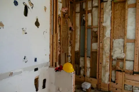 Chantier en cours, murs ouverts révélant l'isolant. Attention, la laine de bois peut présenter un danger si mal manipulée. Casque et gants de protection à proximité.