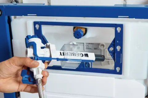 Main d'un plombier installant le mécanisme d'une chasse d'eau encastrée Geberit.