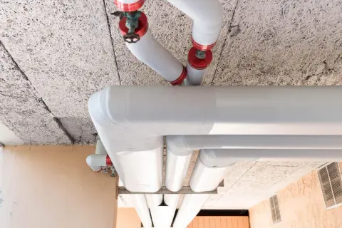 Gros tuyaux blancs, certains avec des capuchons rouges, sont installés sous un plafond texturé. L'ensemble est conçu pour isoler le tuyau de chauffage.