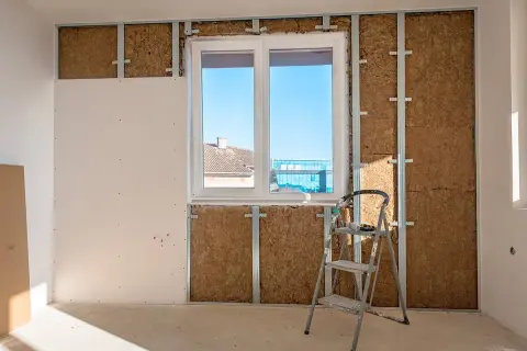 Travaux d'isolation intérieure : murs en cours de pose, avec laine de bois visible derrière une ossature métallique et une plaque de plâtre. Une échelle est présente.