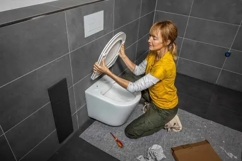 Une femme s'apprête à changer l'abattant WC. Elle tient le nouvel abattant, prête à l'installer sur la cuvette.